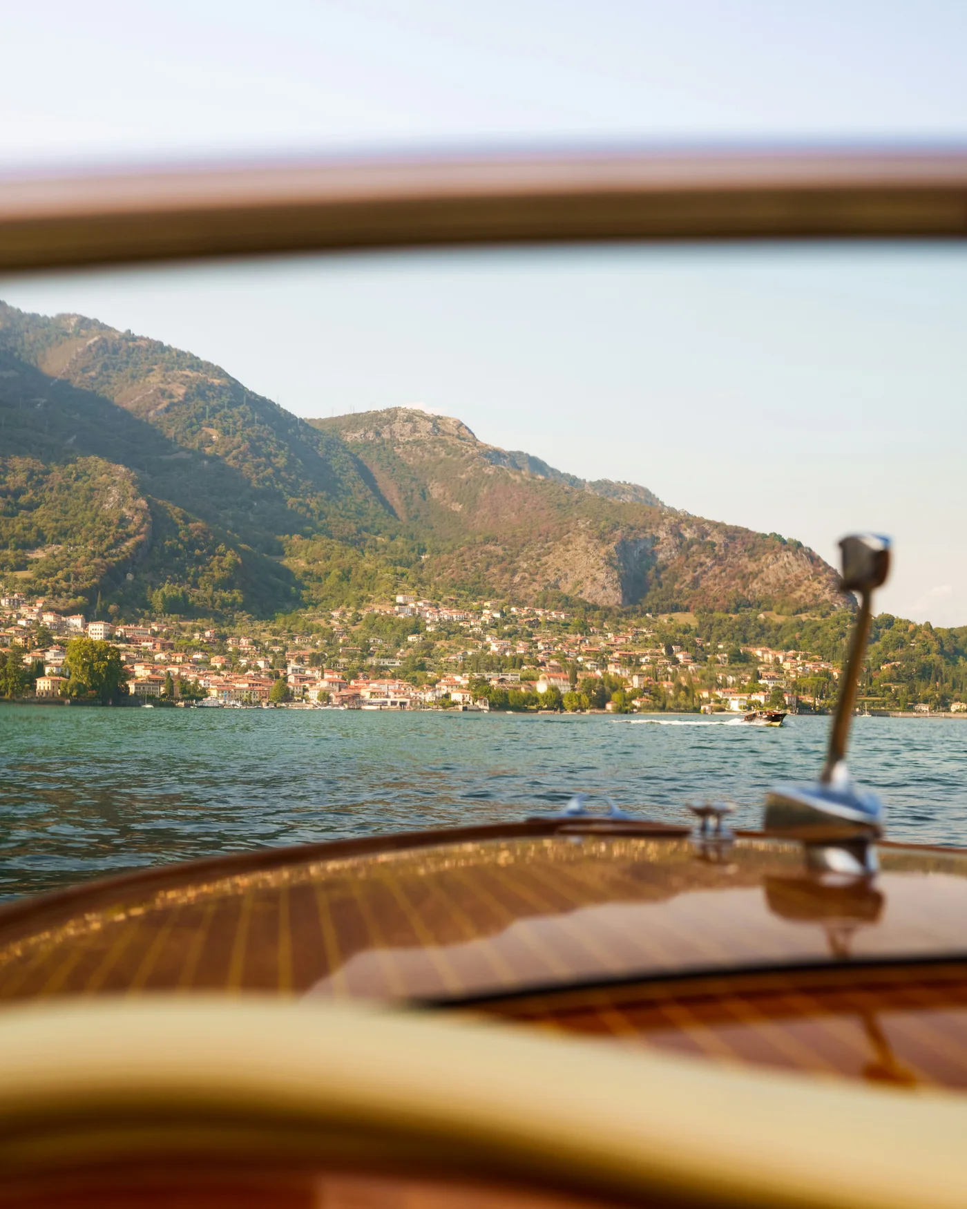 A view from the wooden deck of a vintage motor launch, looking across Lake Como toward a hillside village.